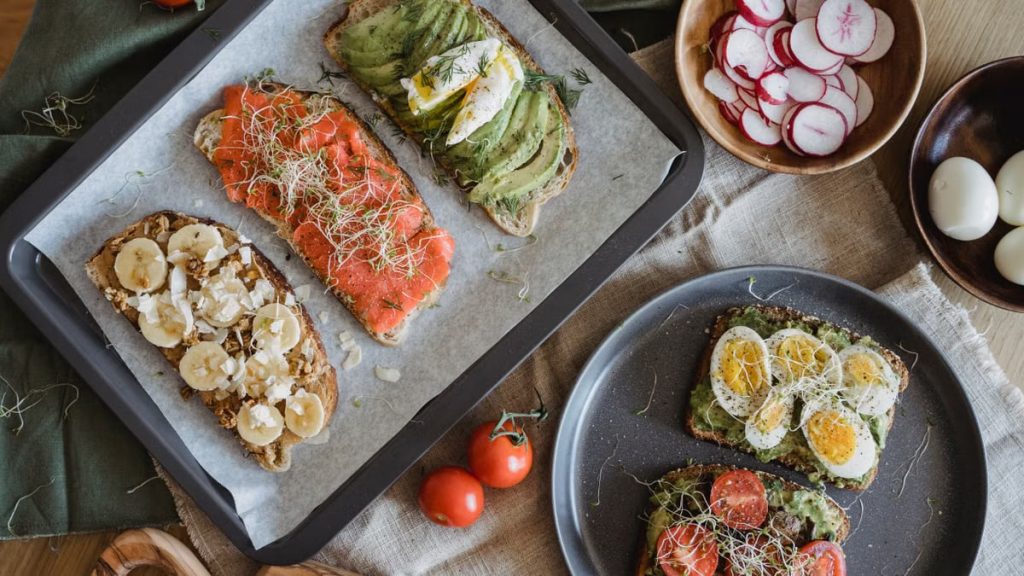 A variety of savory and sweet toasts with avocado, banana, eggs, and fresh toppings on a wooden table.