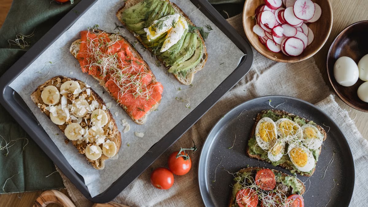 A variety of savory and sweet toasts with avocado, banana, eggs, and fresh toppings on a wooden table.